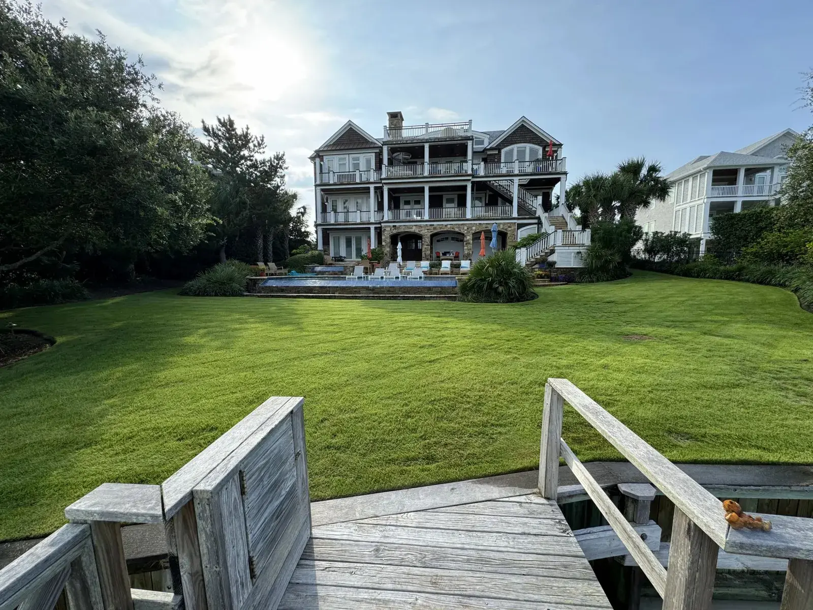 Manicured waterfront lawn sweeping up to a large shingled home and pool